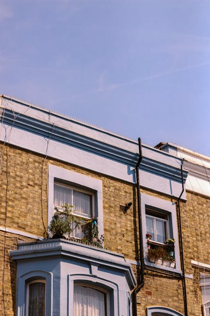 Exterior view of a residential building on Crowndale Estate, Kentish Town, NW5, showing brick walls with white window frames and flower boxes on the windowsills. The roof features modern gutters and downspouts, with a clear blue sky overhead. The building’s facade appears clean and well-maintained, reflecting routine exterior cleaning and maintenance. This image illustrates the typical environment where professional cleaning services by Cleaners Cleaning NW5 focus on surface cleaning and preservation of residential exteriors in the NW5 area.