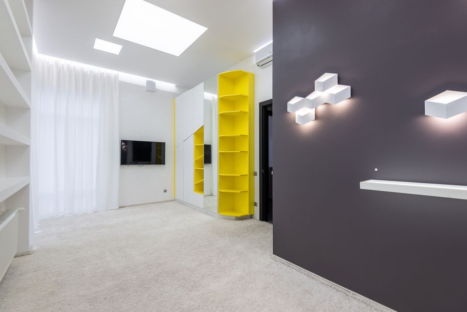 A spacious, modern living room with large floor-to-ceiling windows offering a view of the city skyline in Kentish Town NW5. The room features a light gray L-shaped sofa positioned on a dark gray area 